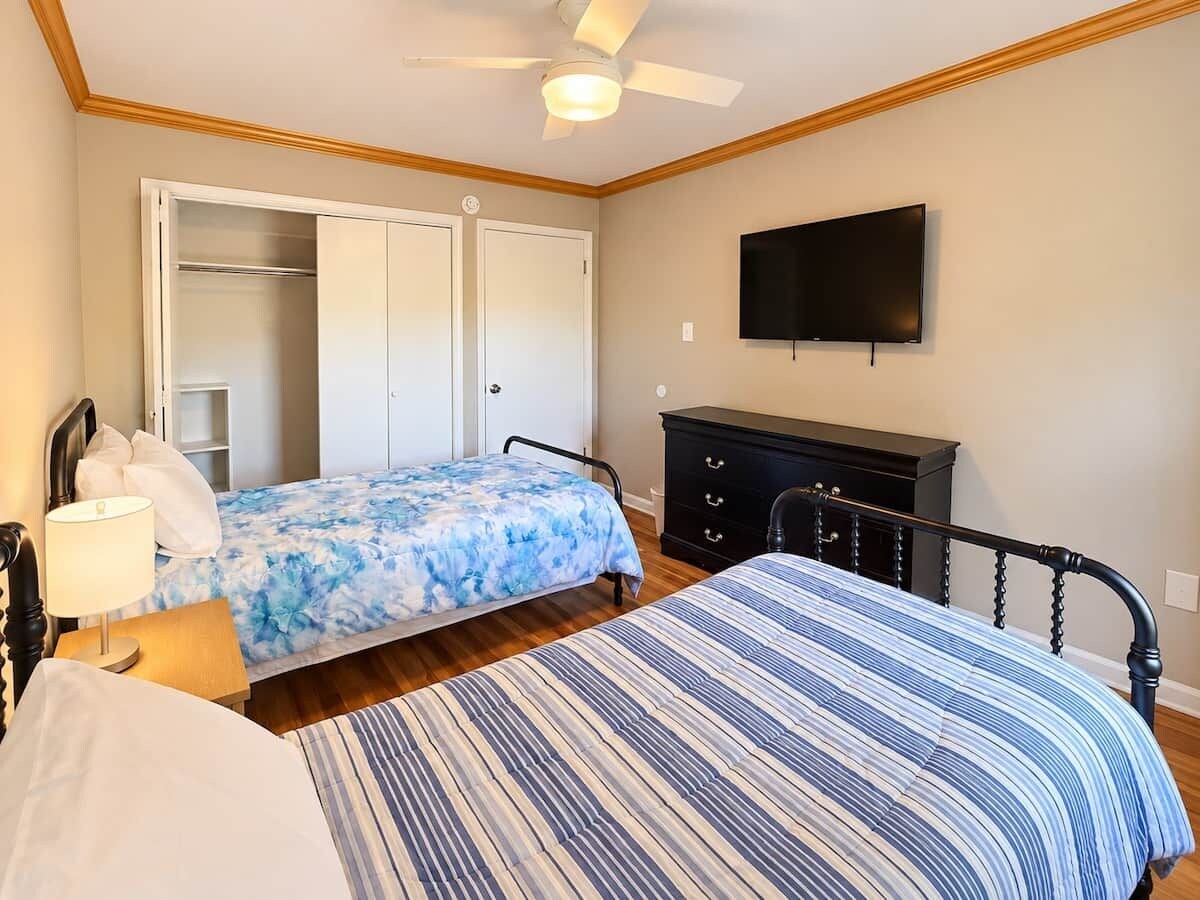 Een slaapkamer met twee bedden, een kledingkast, een televisie en een plafondventilator.