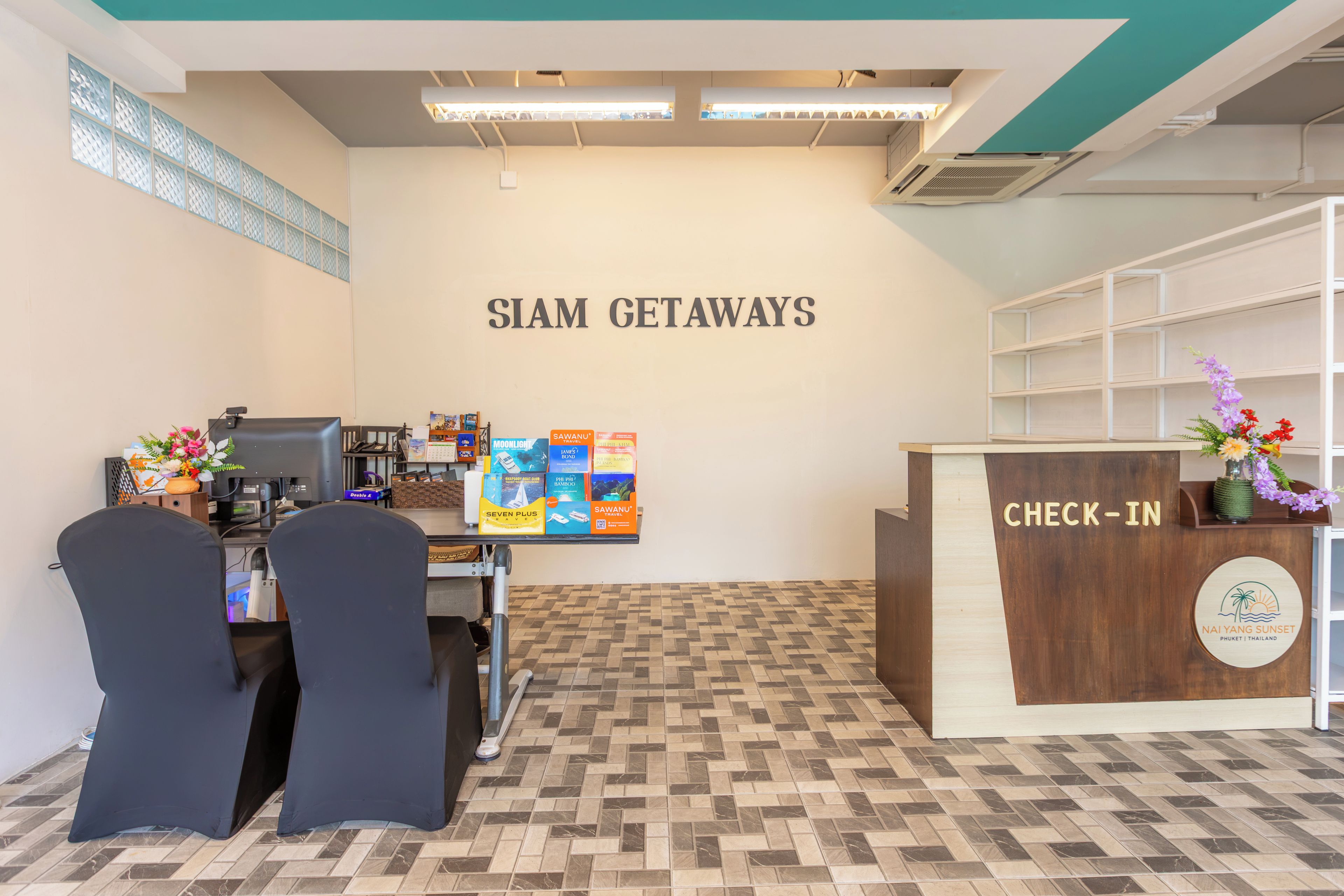 Un área de recepción con mostrador de registro, una pared con el rótulo 'SIAM GETAWAYS' y piso de baldosas.
