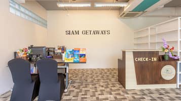 Un área de recepción con mostrador de registro, una pared con el rótulo 'SIAM GETAWAYS' y piso de baldosas.