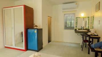 A compact living space with a kitchenette, a wardrobe, a small fridge, a dining area with a table and chairs, and a bathroom with a mirror and window.