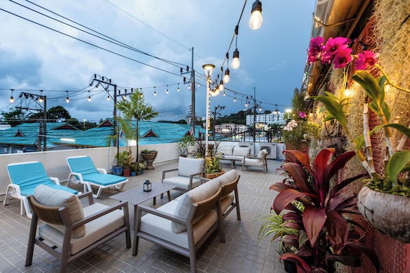 Una terraza en la azotea con asientos al aire libre, luces colgantes y plantas en macetas.