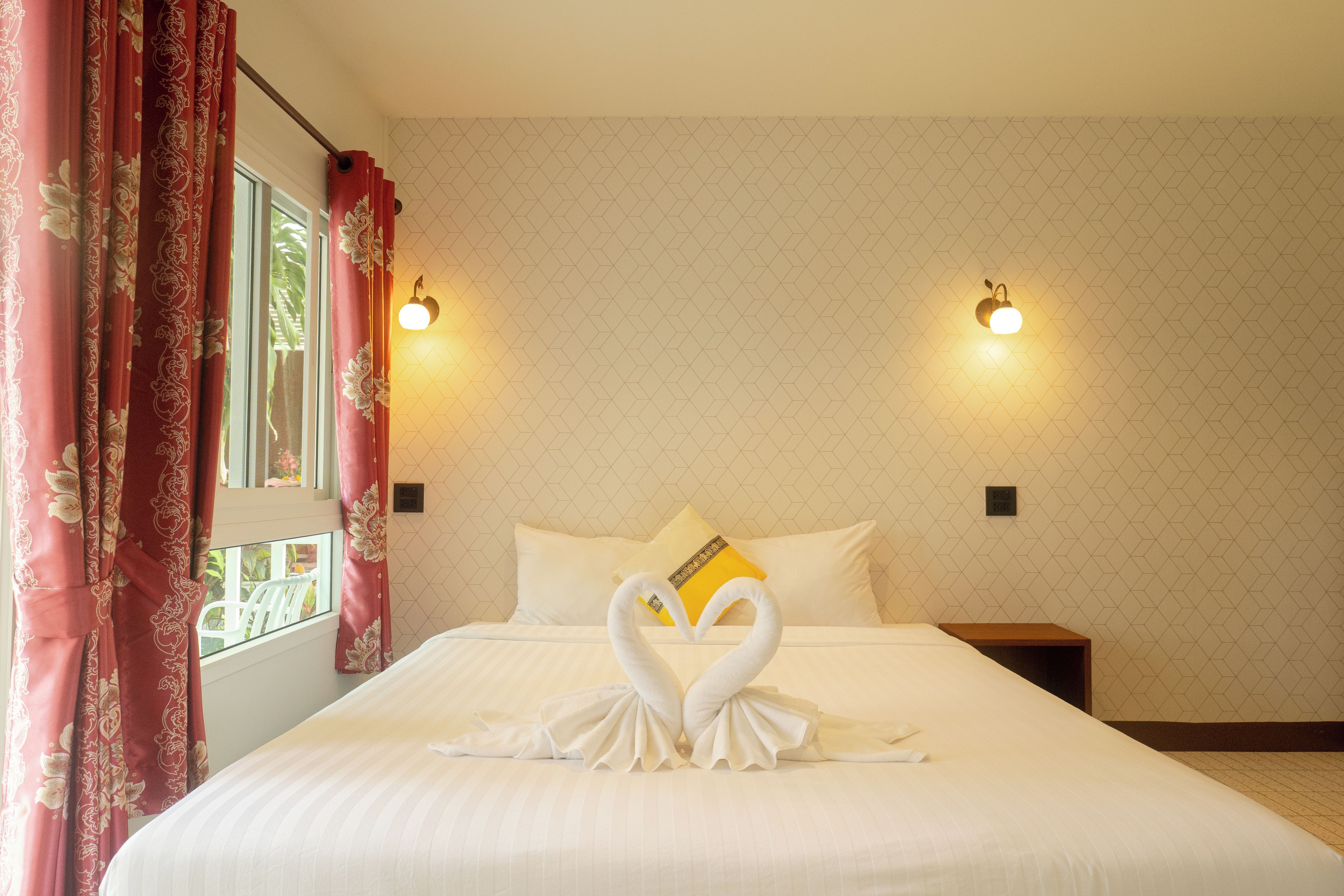A hotel room with a bed, two wall-mounted lights, a window with curtains, and a geometric-patterned wall.