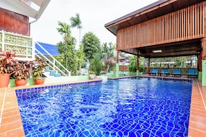 Una piscina con borde de azulejos, rodeada de plantas en macetas y una estructura de madera.