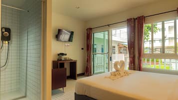 Habitación de hotel con cama, escritorio, televisor y zona de ducha.