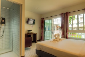 Habitación de hotel con cama, escritorio, televisor y zona de ducha.