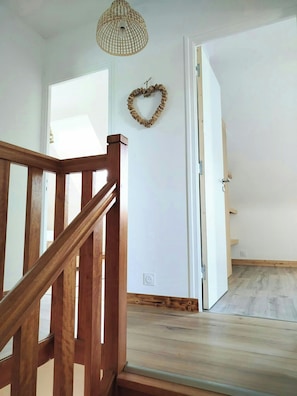 A wooden staircase leading to a room with a white door, a heart-shaped decoration on the wall, and a hanging light fixture. - House with spa and sauna on the Côte des Sables (Cléder)