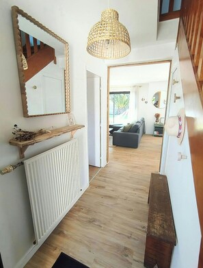 Een gang met een witte radiator, een houten bankje, een spiegel en een hanglamp.
