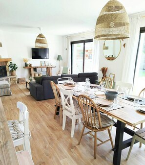 A modern living room with a sofa, dining table set for four, and a television mounted on the wall. - House with spa and sauna on the Côte des Sables (Cléder)