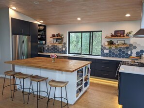Una cocina moderna con una isla central, taburetes de bar y vistas al exterior.