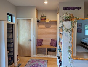 A room with a wooden bench, a shelf with baskets, a mirror, and a door leading to a shoe storage area. - Modern, eco-friendly home with lots of natural light and stunning mountain views (Boulder)