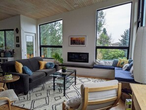 A modern living room with a sofa, coffee table, and a large window with a view of trees. - Modern, eco-friendly home with lots of natural light and stunning mountain views (Boulder)