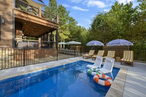 Ein Schwimmbecken mit Liegestühlen und Sonnenschirmen, umgeben von einer Holzterrasse und einem eingezäunten Bereich.