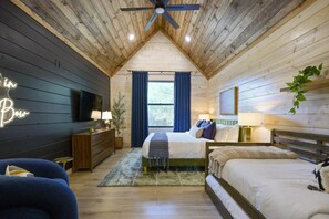 Ein Schlafzimmer mit schrägen Wänden, einem Bett, einem Nachttisch, einer Lampe, einer Pflanze und einem Neonzeichen.