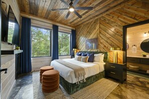 Ein Schlafzimmer mit Holzbalkendecke, einem Bett mit vielen Kissen, einem Nachttisch, einem Spiegel und einem Fenster mit Vorhängen.