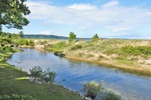 Ein Fluss mit einer Brücke, umgeben von Grünflächen und Hügeln in der Ferne.
