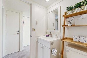 A bathroom with a white sink, mirror, and a shelf with toiletries. - Cozy Retreat on Sleeping Bear Dunes & Lake Michigan Views (Glen Arbor)