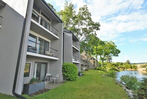 Ein modernes, mehrstöckiges Wohngebäude mit Balkonen, einem Rasen und Blick auf einen Fluss.