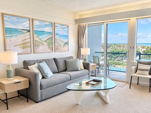 A modern living room with a grey sofa, a glass coffee table, and a view of the ocean through large sliding doors. - Cozy Retreat on Sleeping Bear Dunes & Lake Michigan Views (Glen Arbor)