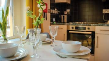 A dining table set with white plates, bowls, and glassware in a modern kitchen with a tiled backsplash and stainless steel appliances.