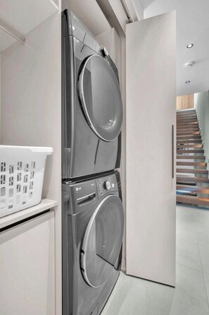 A modern laundry room with stacked washing machines and a white laundry basket. - Miura New Modern Miami | Luxury Villa  4BR 10PPL (Miami)
