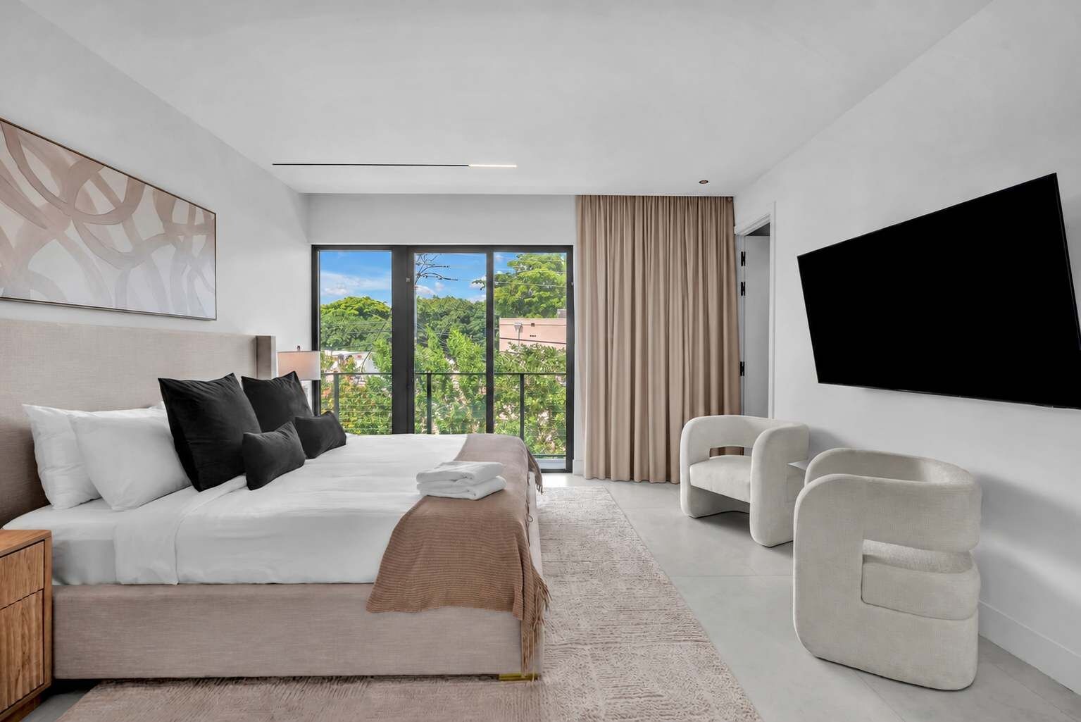 A modern hotel room with a bed, a TV, a seating area, and a balcony with a view.