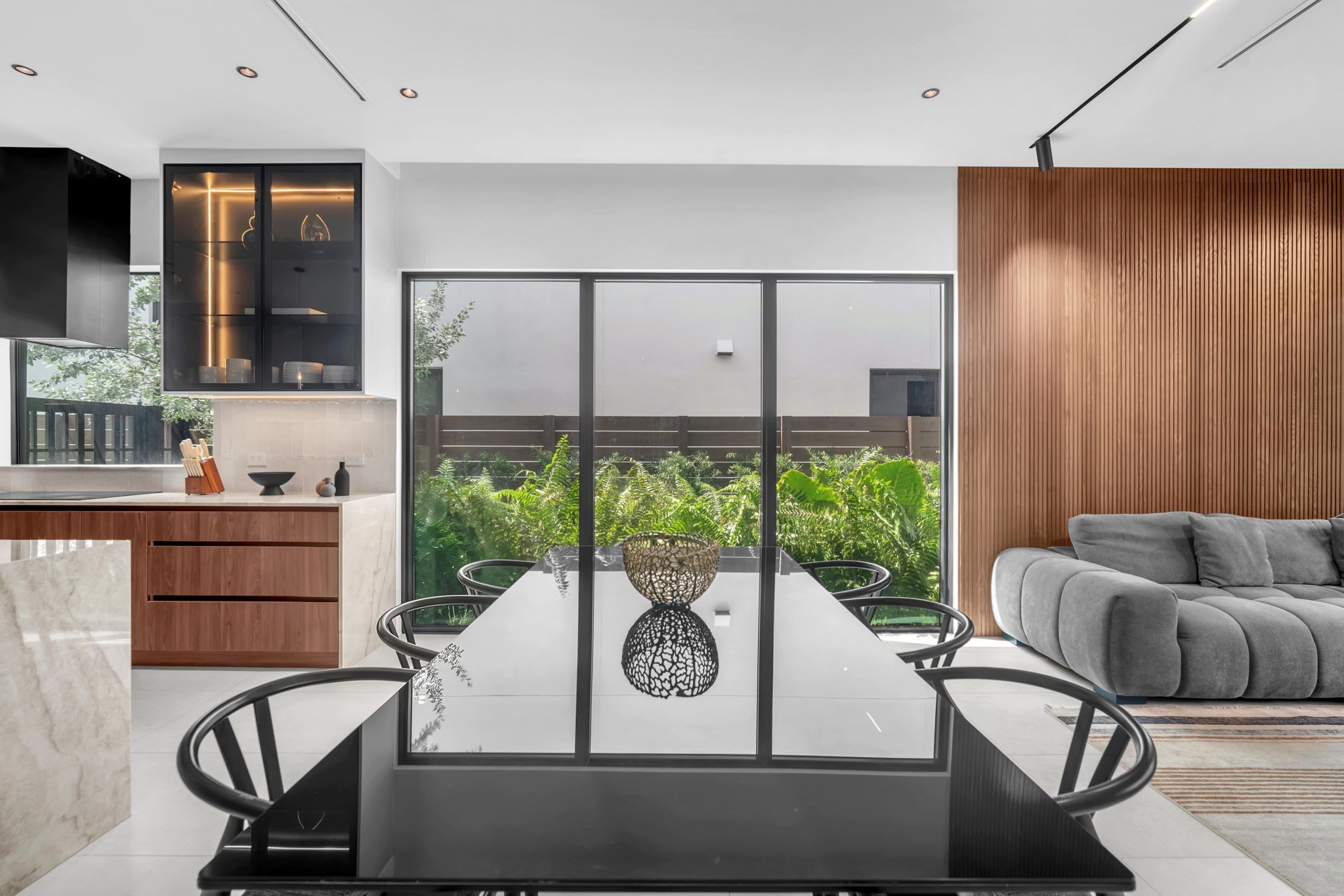Un espace repas moderne avec une cloison en verre, une table à manger avec des chaises et une vue sur la verdure à l’extérieur.