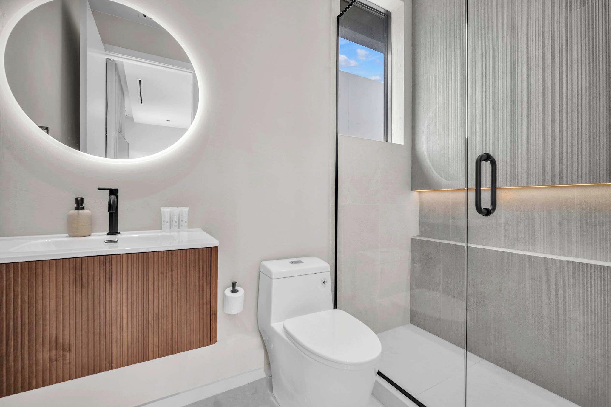 Une salle de bain moderne avec un miroir rond, des toilettes et un espace douche.