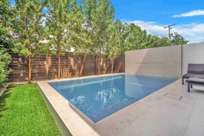 Een rechthoekig zwembad met een houten omheining en bomen op de achtergrond.