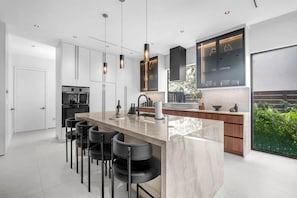 A modern kitchen with a central island, bar stools, and pendant lighting. - Miura New Modern Miami | Luxury Villa  4BR 10PPL (Miami)