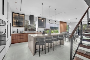 A modern kitchen with a central island, bar stools, and pendant lighting. - Miura New Modern Miami | Luxury Villa  4BR 10PPL (Miami)
