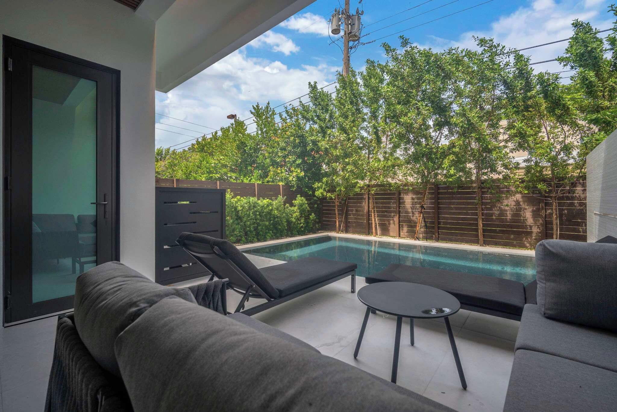 Un espace de vie extérieur moderne, doté d’une piscine, d’un canapé, d’une table et offrant une vue sur le ciel et les arbres.