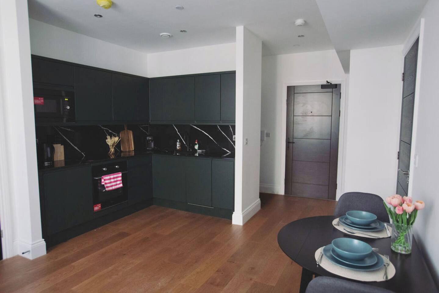 A modern kitchen with dark cabinetry, a wooden countertop, and a dining area with a table set for two.