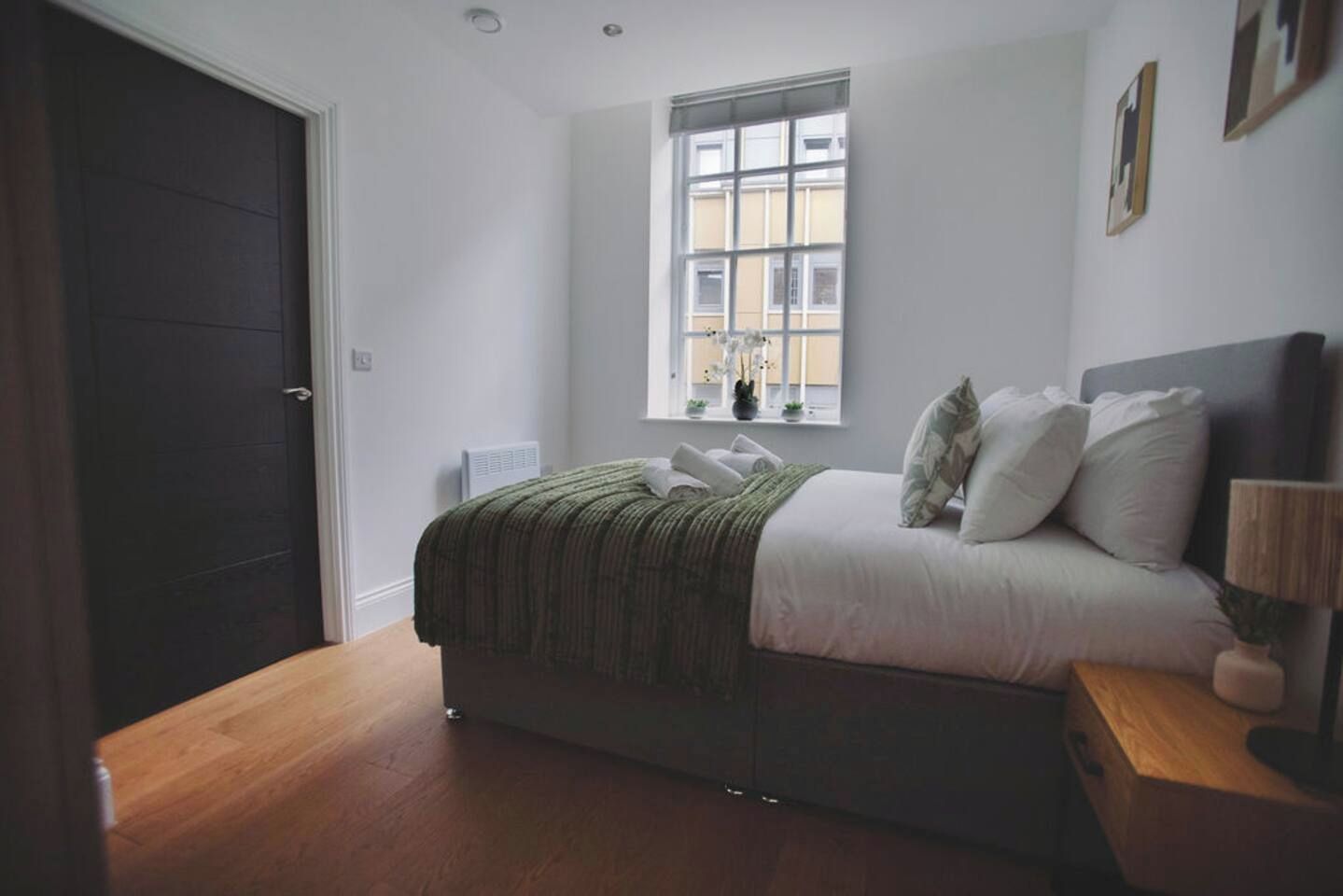 A bedroom with a bed, a window, a nightstand, and a door.