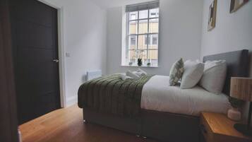 A bedroom with a bed, a window, a nightstand, and a door.