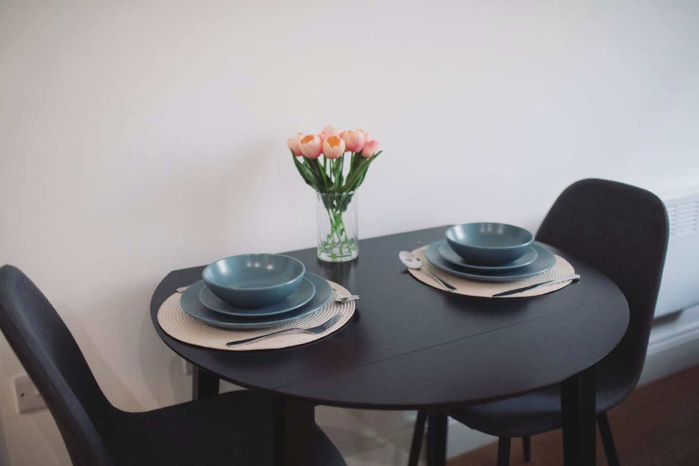 Une table à manger avec deux assiettes bleues, un vase avec des fleurs roses et des chaises noires.