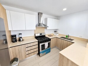 Une cuisine moderne avec des armoires blanches, une hotte de cuisinière en acier inoxydable, une cuisinière à gaz, un four encastré et un évier.