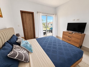 A bedroom with a bed, a television on a wooden dresser, and a sliding glass door leading to an outdoor area. - Ocean View Sunrise 2BR Navio Los Corales C403 (Bávaro)