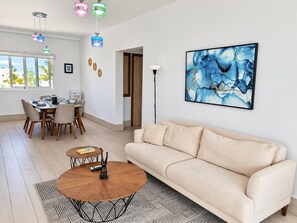 Un salon moderne avec un canapé beige, une table basse et un coin repas comprenant des chaises et une table dressée pour quatre personnes.