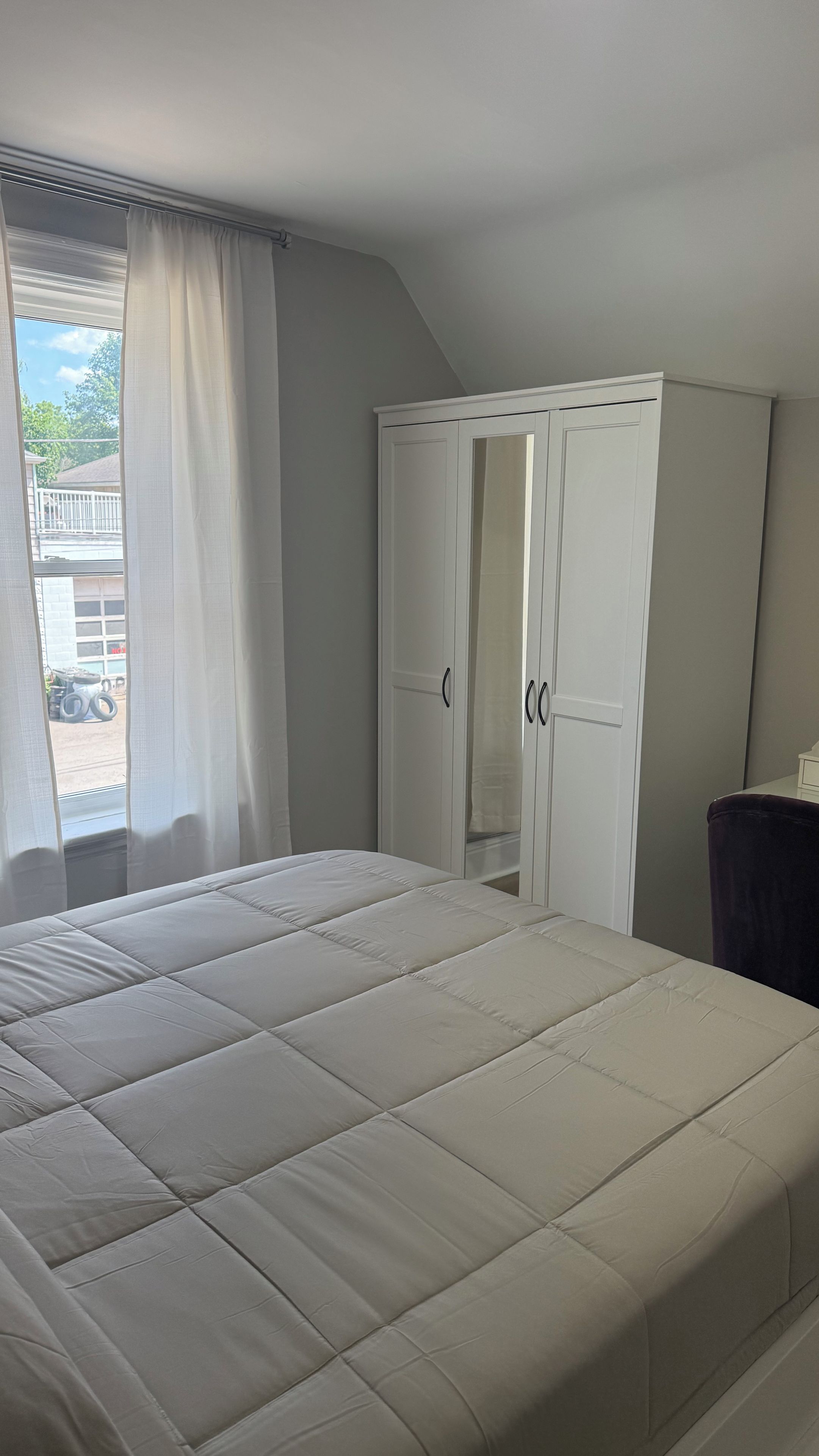 A bedroom with a bed, a wardrobe, and a window with curtains.