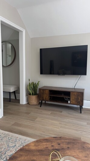 Een woonkamer met een wandtelevisie, een houten dressoir, een ronde spiegel en een potplant.