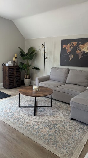 Una sala de estar moderna con un sofá gris, una mesa redonda, una planta grande en maceta, un mapa mundial en la pared y un mueble de madera.