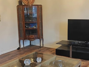 Ein Wohnzimmer mit einem Holzkabinett, einem Glastisch und einem Flachbildfernseher.