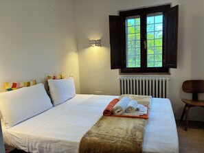A bedroom with a bed, pillows, a rolled-up towel, a radiator, and a window with curtains. - Stunning villa with a pool in the Umbria Valley (Gualdo Cattaneo)