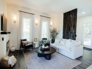 A modern living room with a white sofa, a black coffee table, and a television on a stand. - Dark Skies | Rooftop Deck | Hot Tub | Pond Views | Game Room! (Campton)