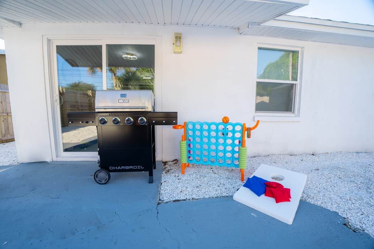 A barbecue grill, a children's play structure, and a white mat with red and blue cloths on a concrete patio.