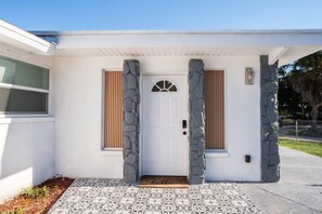 A house with a white exterior, a front door with a doormat, and stone pillars.