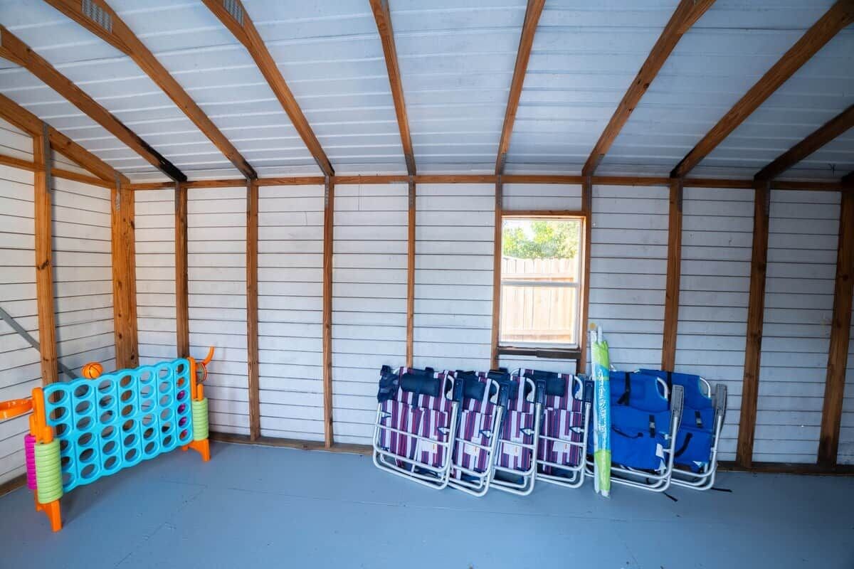 A room with a sloped ceiling, wooden beams, and a window. There are colorful plastic barriers and several folding chairs.
