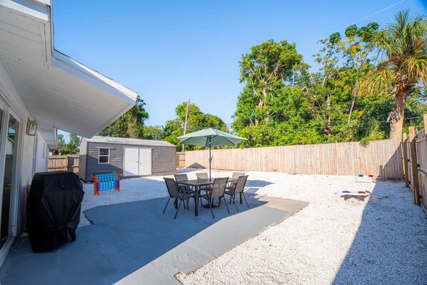 A backyard patio with a table and chairs, a grill, and a covered area.
