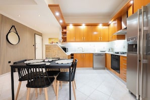 A modern kitchen with wooden cabinets, stainless steel appliances, and a dining area with black chairs and a marble table. - Comfy stay 2br flat 1gbps 4 min walk from metro (Athina)