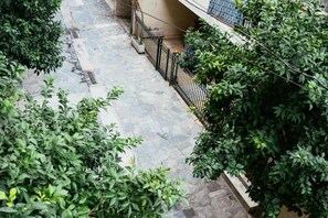 A narrow stone-paved pathway flanked by dense green foliage and a black metal fence. - Comfy stay 2br flat 1gbps 4 min walk from metro (Athina)